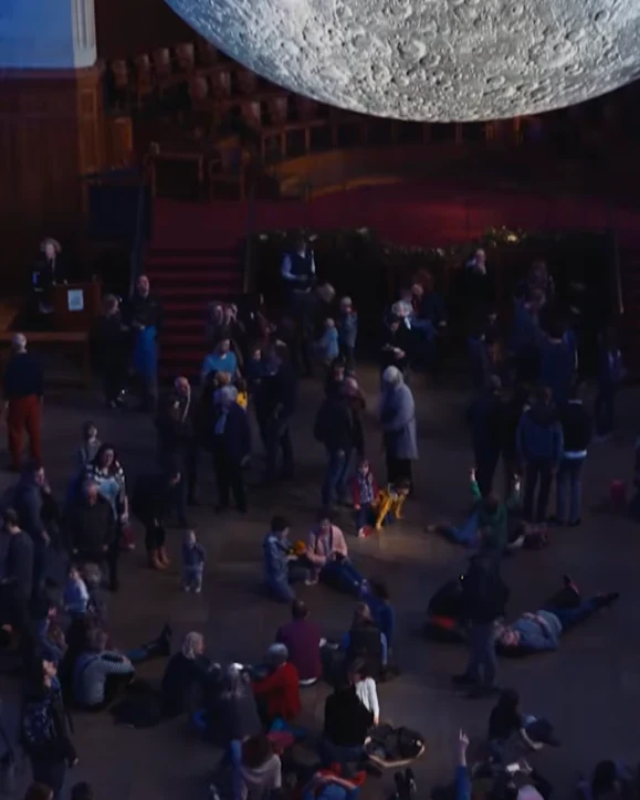 Visitors gathered and lying on the floor beneath the Museum of the Moon