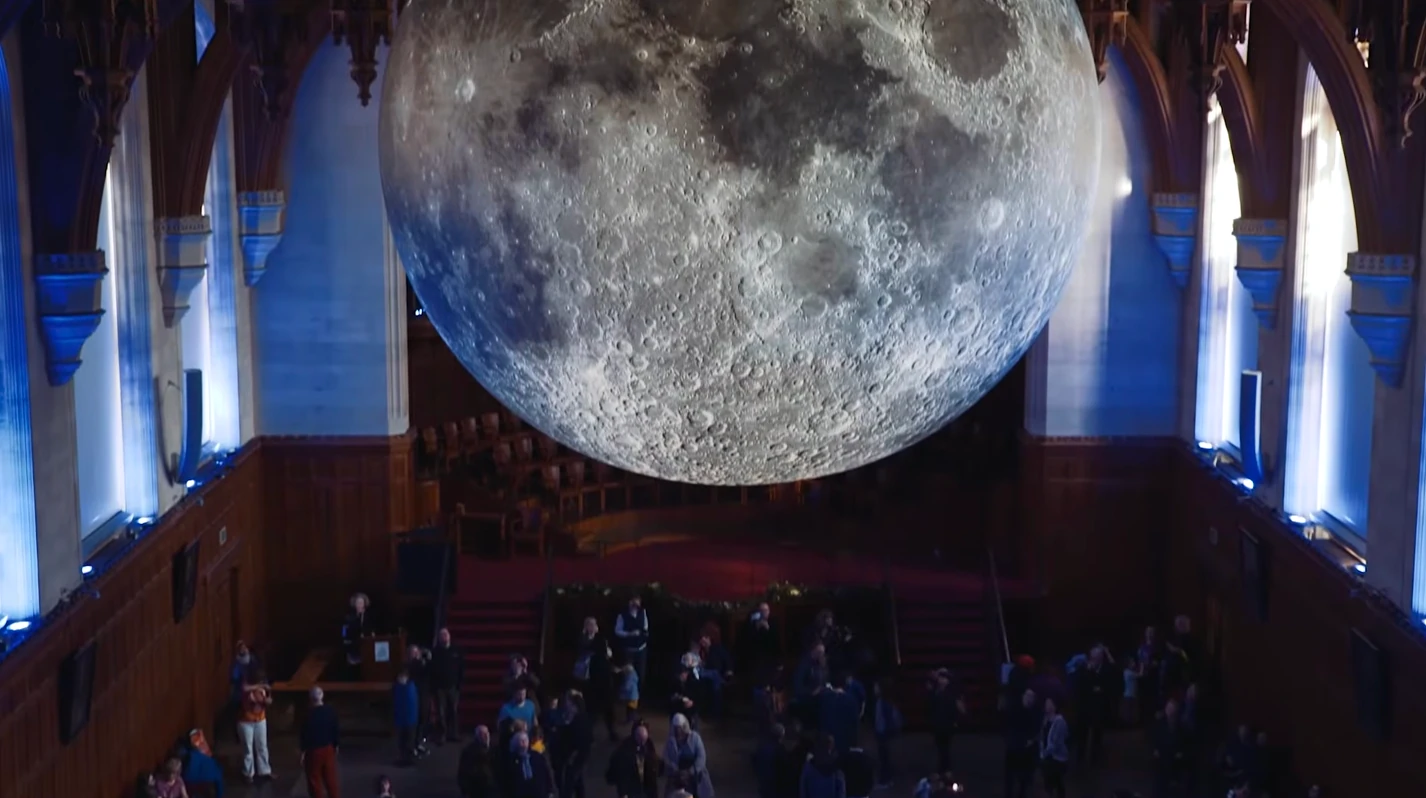 Luke Jerram’s Museum of the Moon hanging in a gothic hall above a crowd of visitors